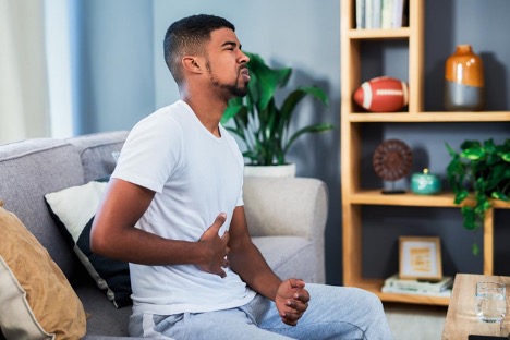 A man holding stomach and experiencing an intestinal infection while sitting on his sofa at home